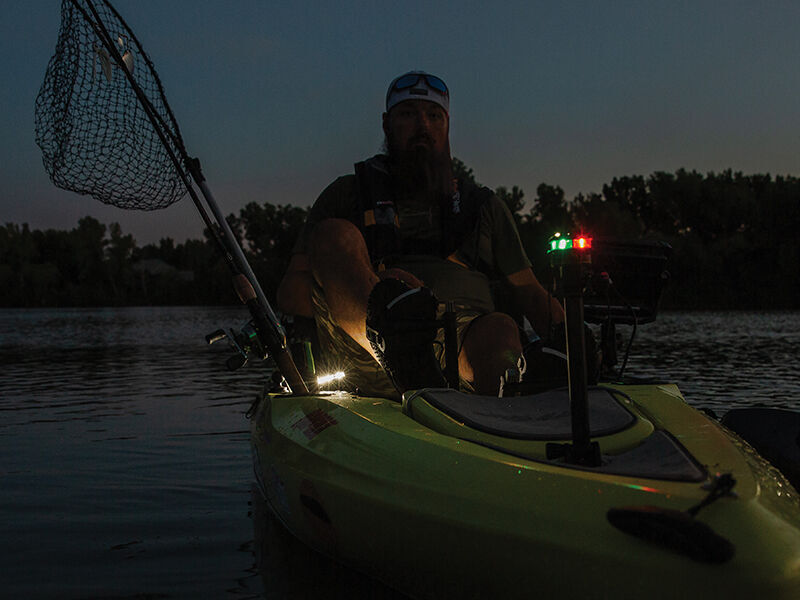 person with fishing gear in small boat with guardian angel light mounted to it