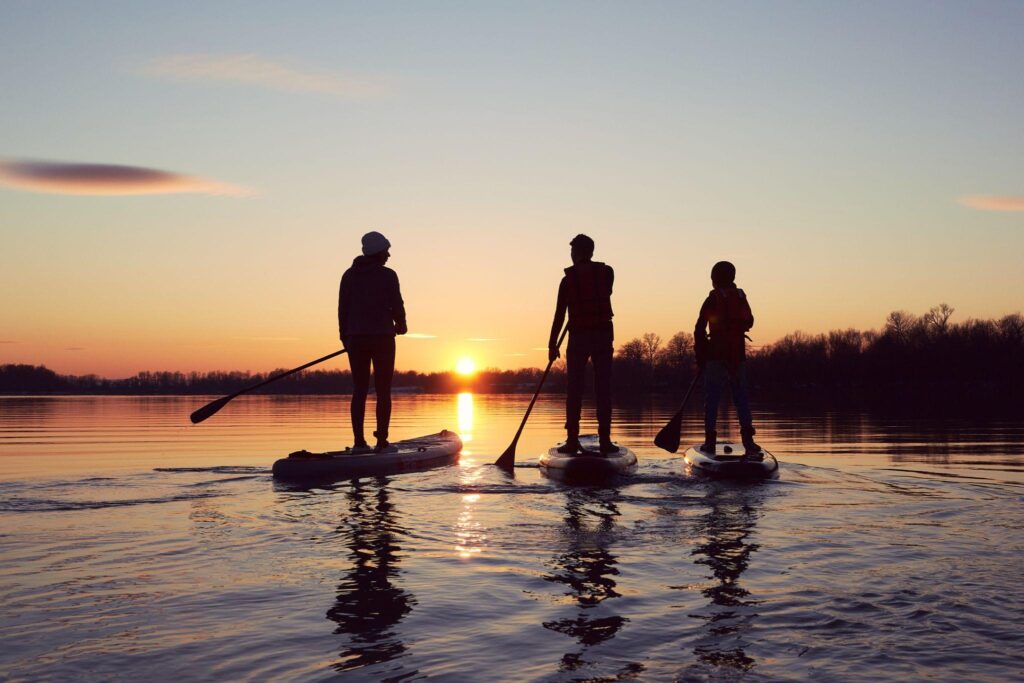 Three people paddleboarding on a lake at sunset